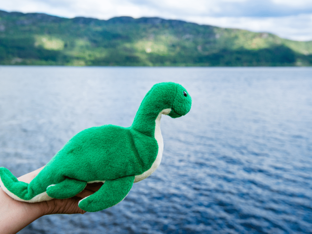 The loch ness monster Loch Ness monster plushie held up in from of Loch Ness
