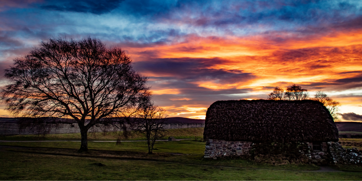 Leanach Cottage at Culloden battlefield silhouetted against a fiery sunset sky