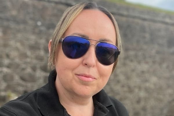 Lesley Kennedy, host of the Everything Scotland podcast, wearing sunglasses against a stone wall background