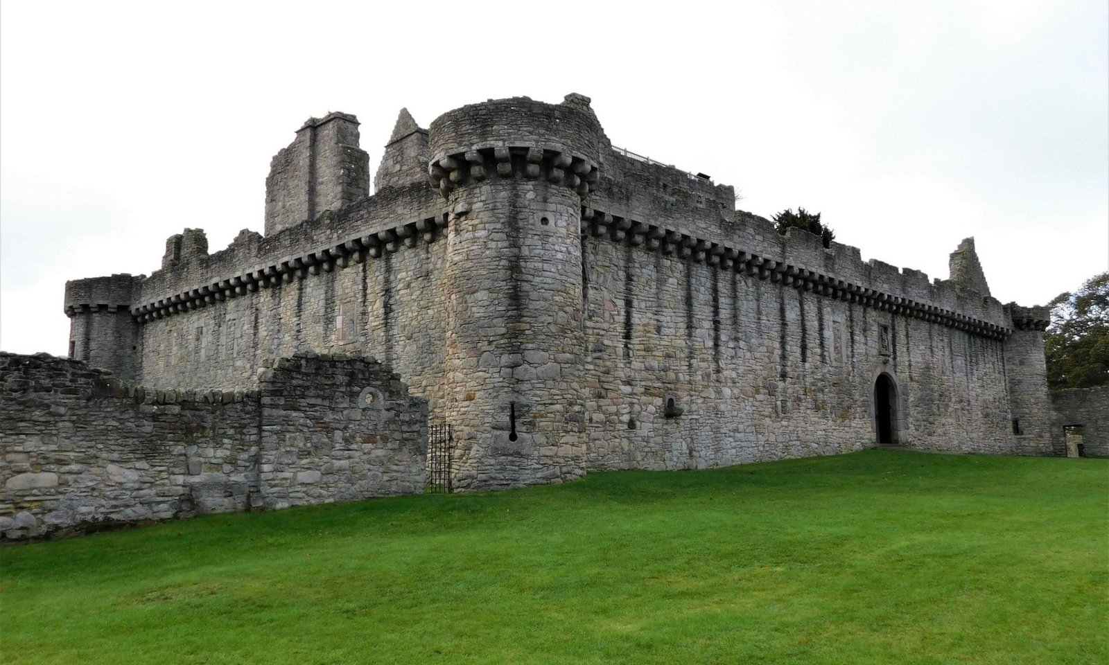 Ruined stone exterior of Craigmillar Castle with corner turret and battlements, set on a grassy slope near Edinburgh