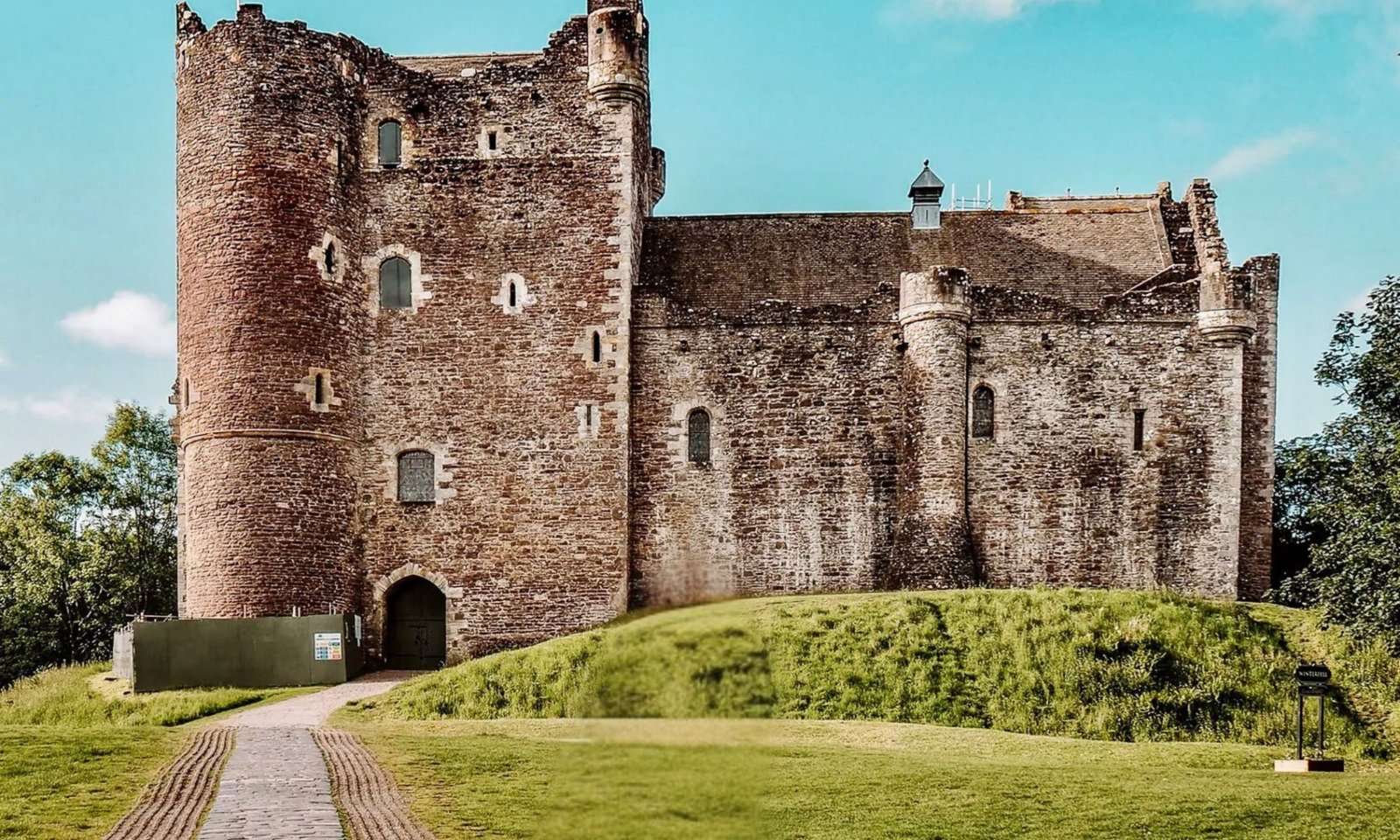 Medieval stone tower and gatehouse of Doune Castle on a grassy mound, with a cobbled path leading to the entrance