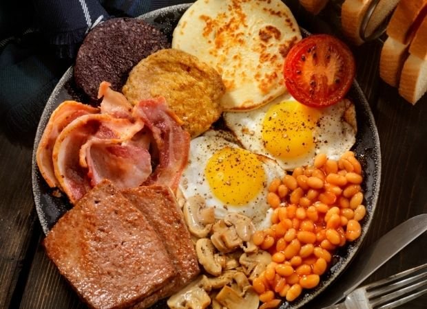 Full Scottish breakfast with black pudding, tattie scone, fried eggs, bacon, sausage, square sausage, beans, mushrooms, and tomato