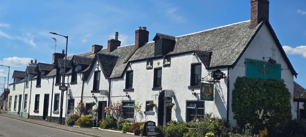 Whitewashed traditional Scottish pub with slate roof, hanging flower baskets, and outdoor seating under a blue sky