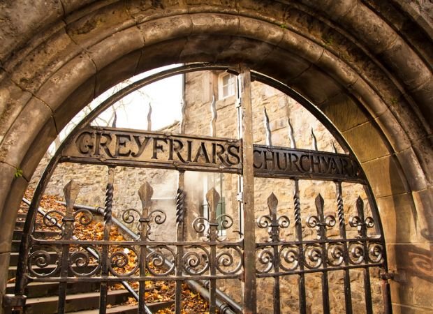 The arched iron gate of Greyfriars Kirkyard in Edinburgh, entrance to the graveyard famous for the Mackenzie Poltergeist and ghost tour stories.